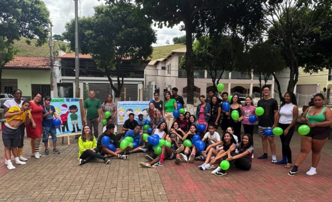Foto de vários estudantes e funcionários reunidos em uma praça, usando meias coloridas e diferentes e segurando balões azuis e verdes