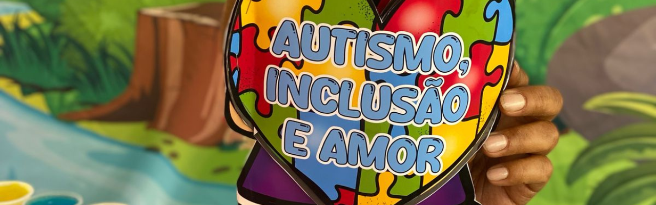 Foto de uma mão segurando uma peça de papel, de um coração com peças coloridas de quebra cabeça, com o texto "Autismo, inclusão e amor"
