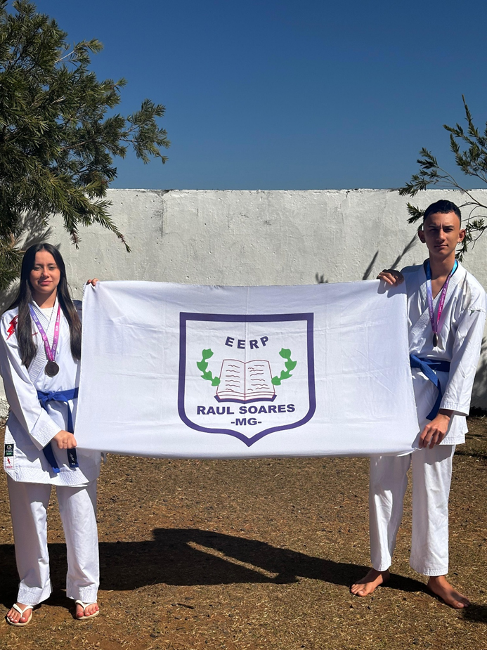 Dois estudantes de kimono segurando uma bandeira da cidade de Raul Soares